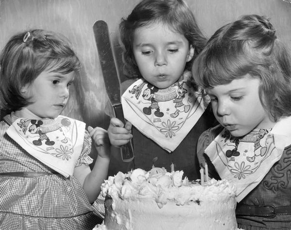 Triplets blowing out the candles of their birthday cake.