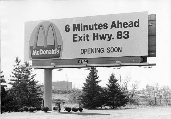 A billboard advertising the opening of a particular McDonald's restaurant. Express highways promoted the emergence of large signs that could be read at a distance by motorists traveling at high speed.