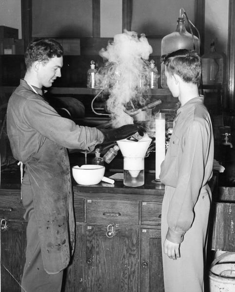 Chemistry experiment by two men being conducted with steam rising from equipment.