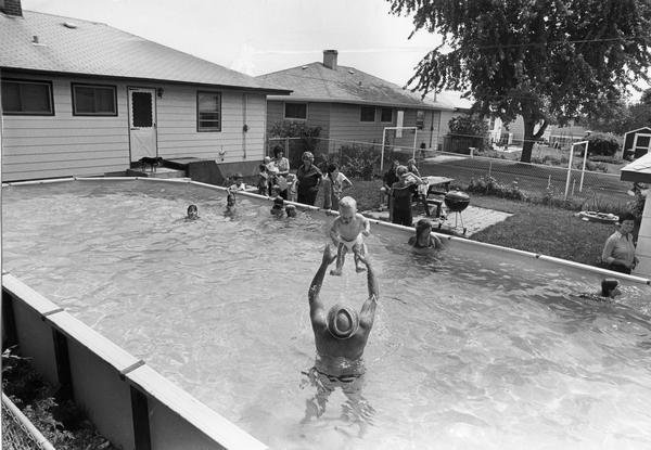 A family relaxes by their backyard pool, while a father tosses his infant son gently in the air.