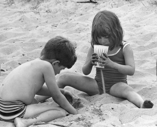 A boy and girl play in the sand at the beach.