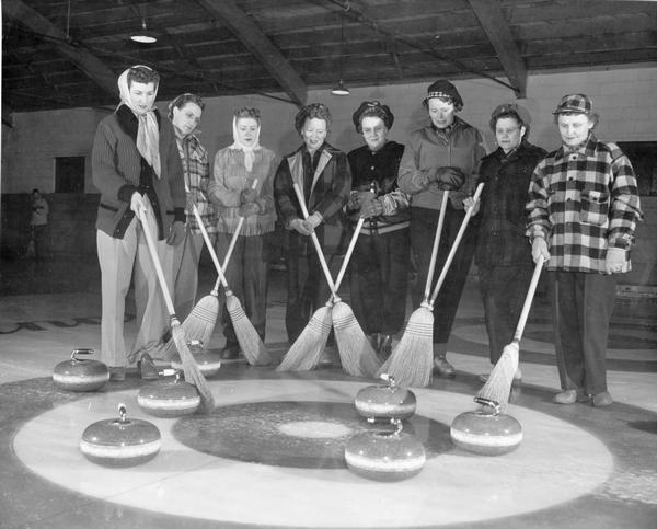 A female curling team poses with their brooms and stones for a portrait.