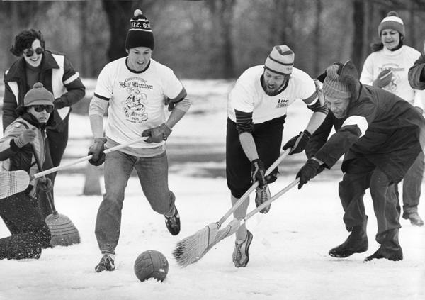 An outdoor broomball game in action in the snow.