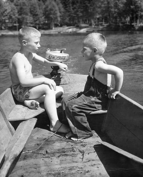 Two boys, probably brothers, using a small boat with outboard motor.