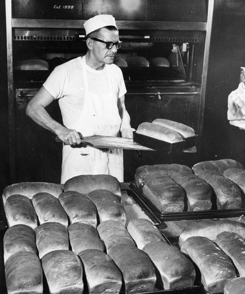 A baker removes multiple loaves of bread from the oven for consumption in both bakery and restaurant.