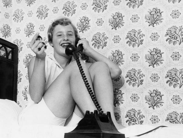 A teenager sitting on a bed talking on the telephone.