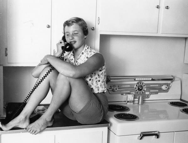 A kitchen counter is a good perch for a teenage girl's telephone conversation.