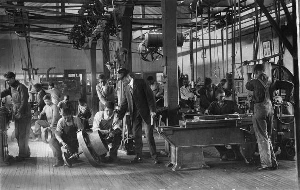The machine shop at the "Normal School for Negroes" or the Tuskegee Institute in action. The students are diligently working at the machinery in the shop.