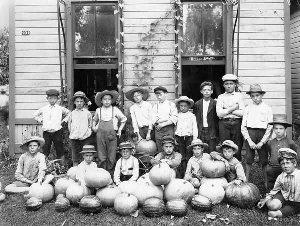 Group of young boys, all wearing hats, posing in front of a building with an assortment of pumpkins and watermelons.
