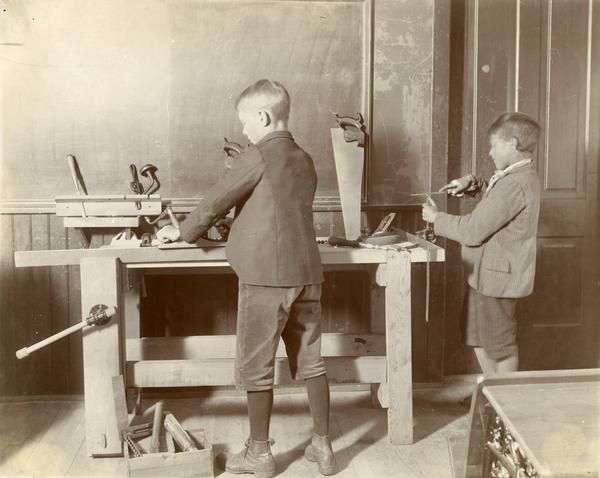 Two boys of different ages using wood tools, including planes and files, during a classroom exercise.