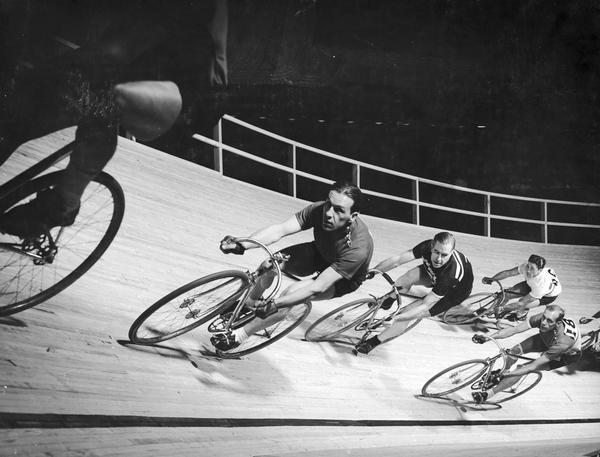 Group of racers bank around a turn on a velodrome track.