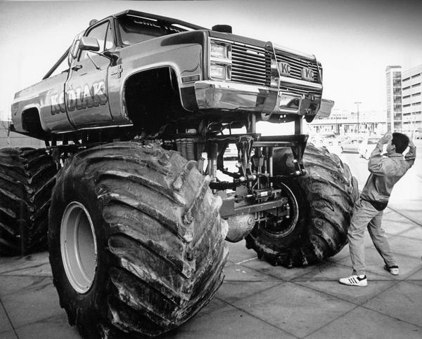 A man cowers in mock awe before Kodiak, a 14,000 pound Ford Silverado rigged with six-foot-tall tires and an extra heavy-duty suspension.  The truck competed in U.S. Hotrod Association Truck Pulls.