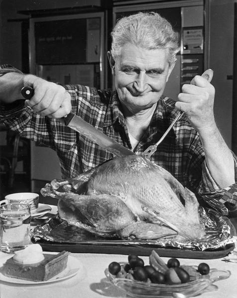 A man takes pleasure in the carving of the Thanksgiving turkey, with other food items in the foreground and vending machines behind him.