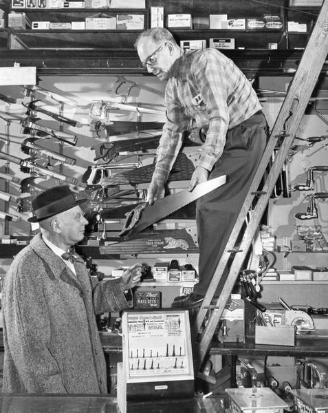 Hilgendorf's Hardware store clerk showing a saw to a customer.