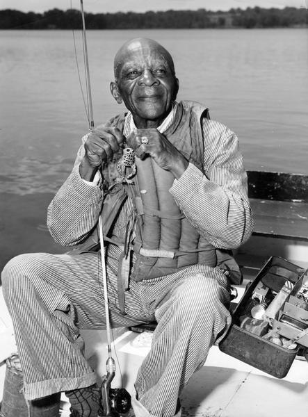 An elderly man looking blissful, sitting in a boat getting ready to cast his line.