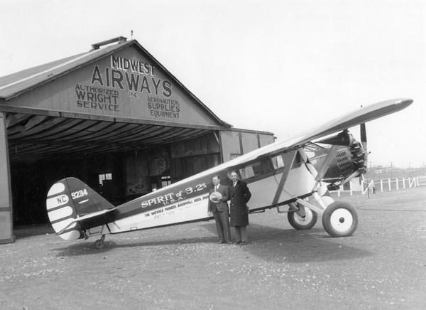 Two men stand next to a small airplane emblazoned with "Spirit of 3.2%" and "The Nation's Pioneer Goodwill Beer Ship" on the side.  They are in front of a Midwest Airways, Inc. hangar that offers "Authorized Wright Service" and "Aeronautical Supplies Equipment".