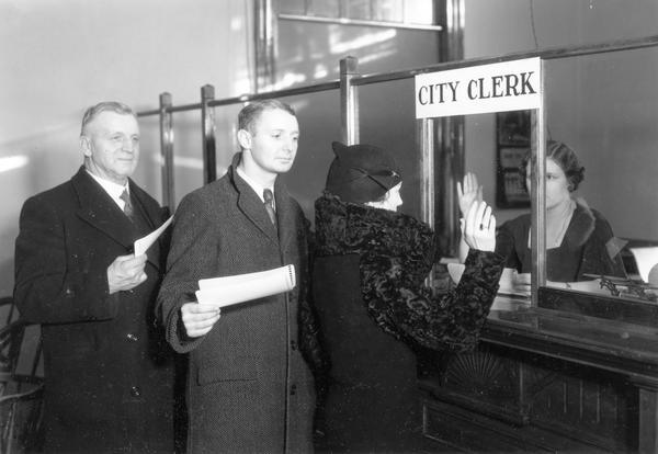 Citizens line up at the City Clerk office to register to vote while a woman raises her hand to take the oath.