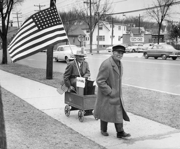 Bet winner and Eisenhower supporter Edwin L. Warner enjoys his payoff from bet loser and Adlai Stevenson backer John Shaat, as Shaat tows Warner along the sidewalk in a wagon.