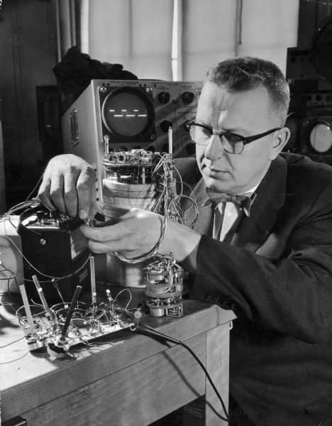 "Doc" Edgerton adjusts equipment in the lab. Known for his pioneering work in the development of the electronic flash, his photograph of a splashing milk-drop is his best known work.