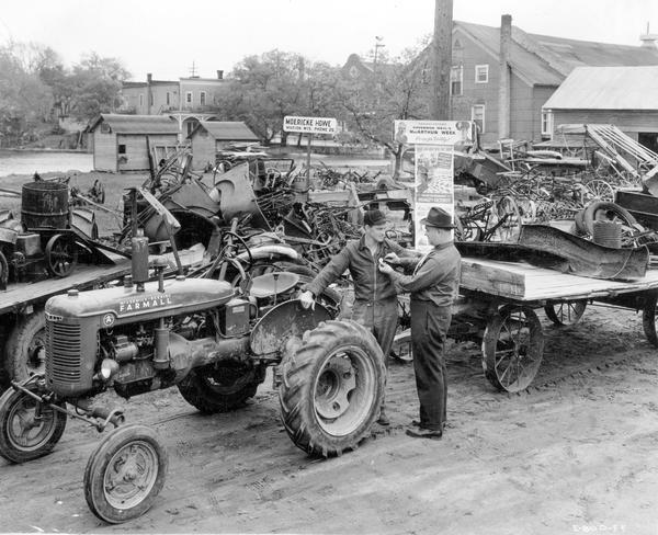 Scrap drive at International Harvester dealer. Original caption: "C.J. Moericke, who is dealer at Marion in the Green Bay territory, was receiving scrap from farmers in a stock pile to the rear of his establishment. Shipments by motor truck from this pile were made to junk dealer at Appleton. Some 15 tons of scrap were in the pile when pictures were taken. Mr. Moericke said he figured on handling a total of about 40 tons. The community was also building up a pile. Mr. Moericke is shown . . . pinning MacArthur button on Harold C. Kruger, who had just brought in a trailer loaded with scrap with his father's Farmall A."