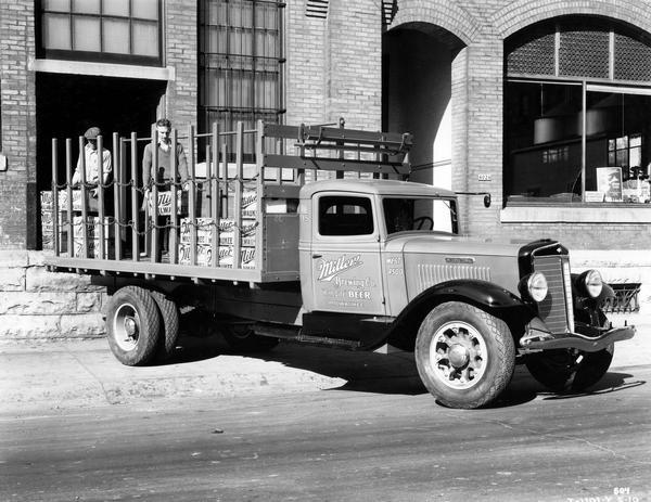 Two men loading cases of Miller beer onto an International C-50 "stake body" truck. The truck was owned by Miller Brewing Company.