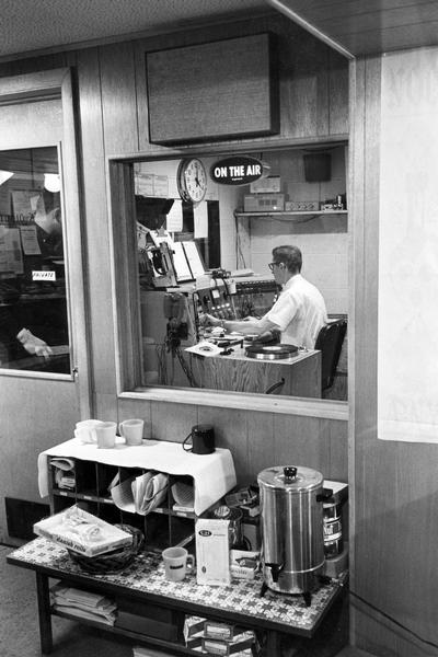Radio announcer Del Viney on the air inside Wisconsin's Very Live Radio (WVLR) station during the dinner music show. Caption reads: "Dinner Music Show is announced by Viney, whose meal usually comes from snack table."