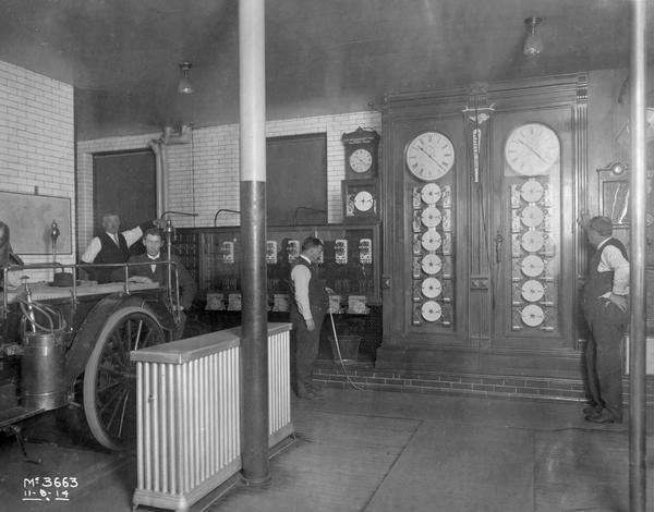 Four men inside the clock and ticker room at International Harvester's McCormick Works. A Chicago White Sox pennant is hanging between two of the clocks. The McCormick Works was built by Cyrus McCormick in 1873 and became part of International Harvester in 1902. The factory was located at Blue Island and Western Avenues in the Chicago subdivision called "Canalport." It was closed in 1961.