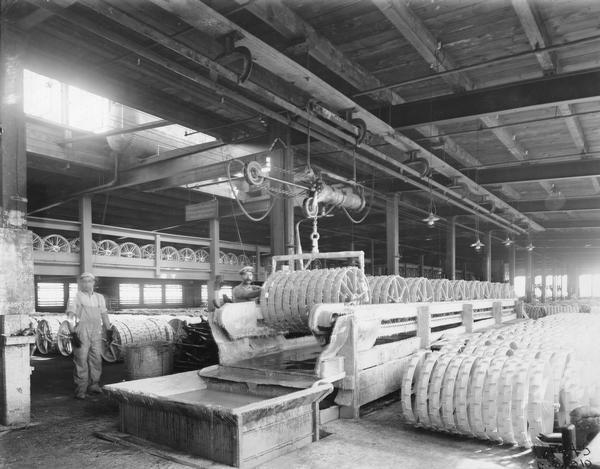 Two men dipping mower wheels in cream color paint at International Harvester's Deering Works (factory). The factory was originally built by William Deering for the Deering Harvester Company in 1880. In 1902 it became International Harvester's Deering Works. The factory was located at Fullerton and Clybourn Avenues and closed in 1933.
