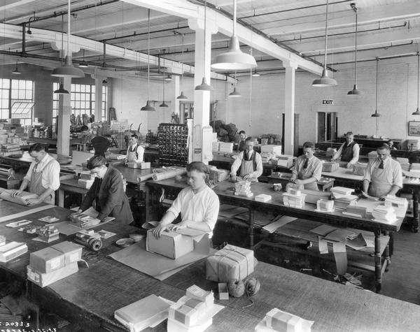 Employees packaging company publications for shipment in a warehouse. The warehouse is possibly part of Harvester Press. Publications may include advertising literature and Agricultural Extension publications.