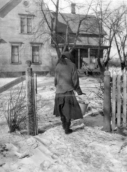 Woman carrying a bucket of water back to her farmhouse in winter.