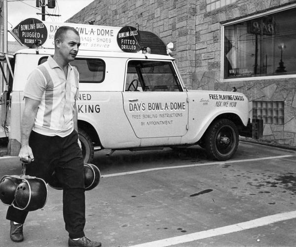 Man delivering serviced bowling balls from an International Scout truck. The truck was owned by Day's Bowl-A-Dome.