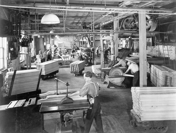 Slightly elevated view of workers manufacturing, finishing and assembling wooden wagon components at International Harvester's Chatham Works in Ontario, Canada. The factory was owned and operated by the Chatham Manufacturing Company until it was purchased by International Harvester in 1910. The factory produced wagons, sleighs and eventually trucks (1921).