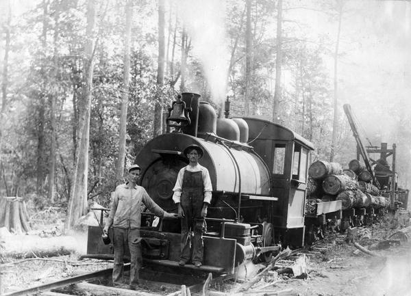 Two workers are posing in front of a steam engine carrying logs for an International Harvester sawmill.