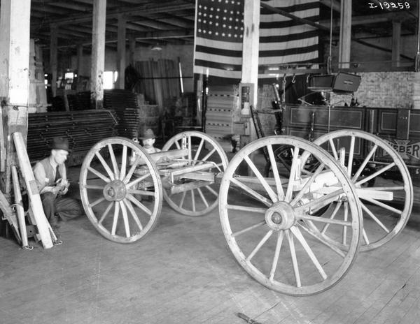 Men working on a wagon truck inside International Harvester's Weber Wagon Works. A completed Weber wagon and a large American flag are in the background. The factory was located at Auburn Park and was owned by the Weber Wagon Company until 1904. International Harvester produced wagons at the factory until 1927.