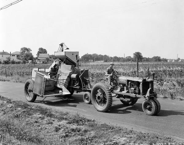 Farmer driving a McCormick-Deering Farmall F-20 tractor and combine (harvester-thresher) on a rural highway. The tractor and combine were equipped with Firestone tires, and were moving from one farm to another at Purdue University.