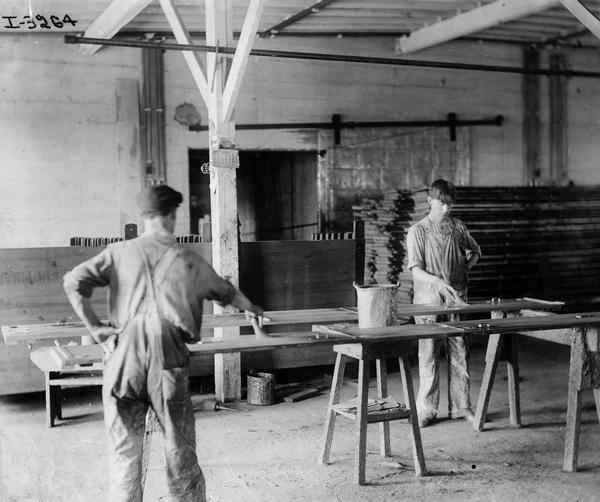 Two workers painting, varnishing or otherwise treating wood planks at International Harvester's Weber Works in Auburn Park. The factory was owned by the Weber Wagon Company until International Harvester purchased it in 1904.