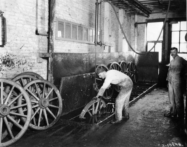 Workers dipping wagon wheels in boiled linseed oil(?) at International Harvester's Weber Wagon Works in Auburn Park. The factory was owned by the Weber Wagon Company until 1904, when it was purchased by International Harvester.