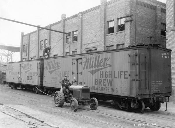 Two workmen use a McCormick-Deering I-30 industrial tractor to attach railroad cars carrying Miller High Life beer.
