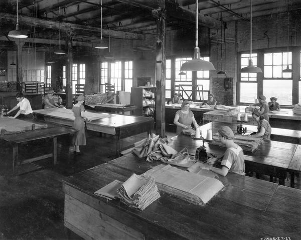 Slightly elevated view of women workers measuring, cutting and sewing sections of canvas for binder back curtains, combine hoods and curtains, burlap bags, combine grain pads, and other items at International Harvester's McCormick Works. The factory was built in 1873 and was located at Blue Island and Western Avenues in the Chicago subdivision called "Canalport." It closed in 1961.