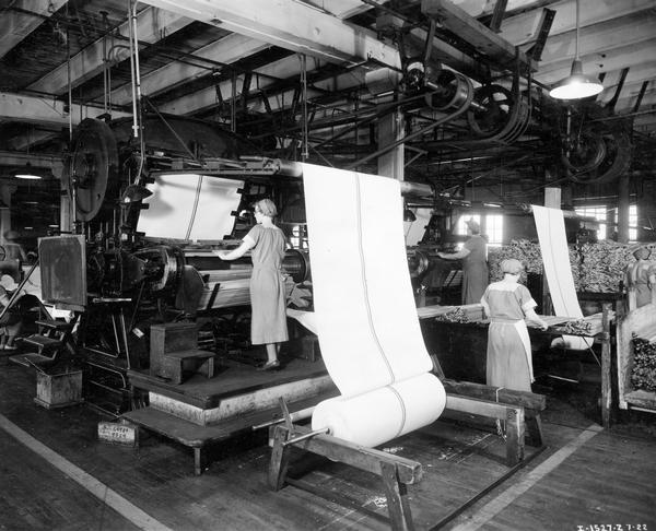 Female workers operating machines to insert wooden slats into binder canvas at International Harvester's McCormick Works. The McCormick Works was built by Cyrus McCormick in 1873 and became part of International Harvester in 1902. The factory was located at Blue Island and Western Avenues in the Chicago subdivision called "Canalport." It was closed in 1961.
