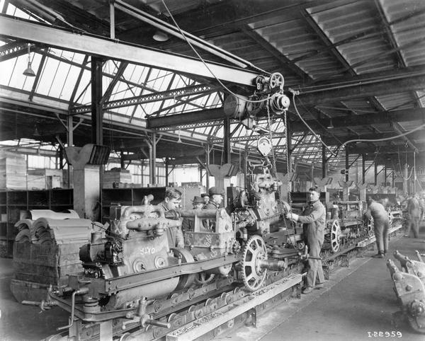 Workers using a jib crane to lower engines into an International 8-16 tractor chassis on an assembly line at International Harvester's Tractor Works.