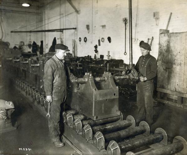 Two men working on engine components on an assembly line at International Harvester's Milwaukee Works. The factory was owned by the Milwaukee Harvester Company before 1902.