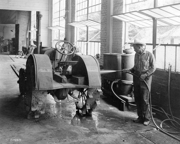 Man washing the grime off a McCormick-Deering 10-20 tractor in the service department of an International Harvester dealership.