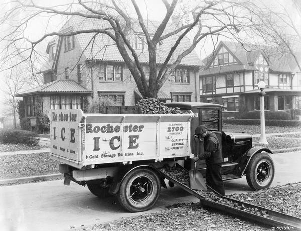 Worker unloading coal from a truck onto a chute on Seneca Parkway in Rochester. The chute appears to be leading to a residential home.  However, there is currently a central median green space at that location and it is likely that the photo was staged. The house at right is at 2 Seneca Parkway. The truck is an International Model S-26 with the name "Rochester Ice and Cold Storage Utilities, Inc." painted on the side.