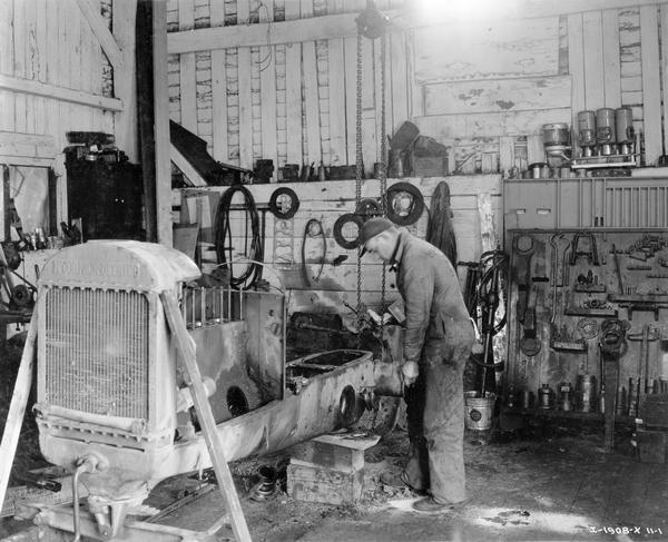 Mechanic at work on the back end of a disassembled McCormick-Deering tractor inside a local International Harvester dealership service department.