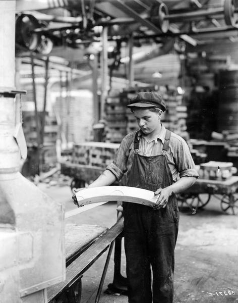 Young man - possibly a teenager - sanding a section of a wooden wagon wheel with a belt sander at International Harvester's Accurate Engineering Works.
