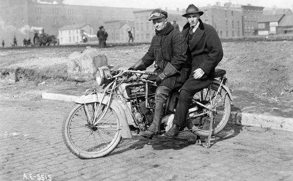 Two riders on an early Excelsior-Henderson motorcycle near a community garden at Harrison and Jefferson streets in Chicago. An International Harvester tractor is cultivating the soil in the background. The men on the motorcycle were the garden inspector and his assistant. The Excelsior-Henderson motorcycle was manufactured in Chicago until it went out of production in 1931.