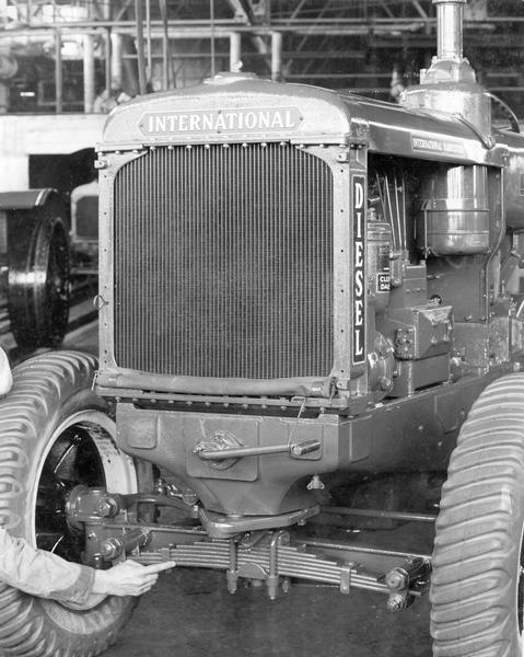 Detailed view of the front of an International ID-40 diesel industrial tractor at International Harvester's Tractor Works. A man is pointing to the tractor's front suspension.