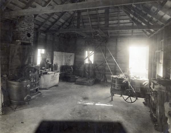 Interior of a farm shed showing a small gasoline engine, wash tub, feed grinder and other equipment powered by a system of pulleys and belts.
