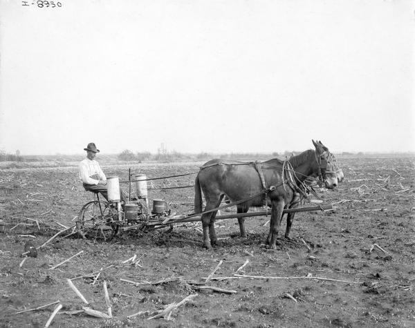 Farmer operating an International Harvester corn planter with fertilizer attachment drawn by two horses or donkeys. The photograph was taken for, or compiled by International Harvester's Agricultural Extension Department.